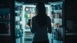 © Oulaphone - A woman standing in front of an open fridge late at night, grabbing unhealthy snacks. Unhealthy food concept.