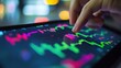 © somneuk - A close-up of a hand analyzing financial charts on a tablet, focusing on stock market trends and investments