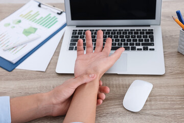 Canvas Print - Man suffering from pain in wrist while working on laptop at wooden table, closeup. Carpal tunnel syndrome