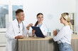 © New Africa - Professional receptionist and doctor working with patient at wooden desk in hospital