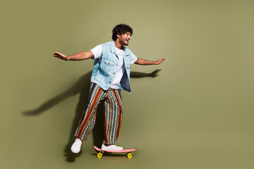 Full size photo of handsome young guy have fun skateboard wear trendy jeans outfit isolated on khaki color background