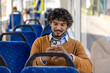 © Liubomir - Man sitting on bus using smartphone with a smile. Casual setting in public transport with blue seats and window light. Engaged and relaxed moment captured.