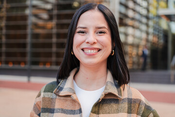 One hispanic woman looking at camera with friendly expression. Close up individual portrait of a latina female smiling, standing outside and staring front. Headshot of a pleased teenage latin girl