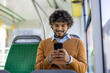 © Liubomir - Young man sitting on bus using smartphone, smiling and engaged in digital content. Casual attire and relaxed atmosphere emphasize modern urban lifestyle and connectivity during commute.