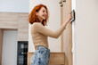 © KIFOR PRODUCTION - Smiling Curly Redhead Girl Looking into Intercom, Anticipating a Warm Greeting