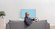 © Ljupco Smokovski - Mature man holding a football and sitting on a sofa in front of a tv screen