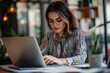 © Nima - A young woman wearing glasses is concentrating on her work on a laptop in a coffee shop, symbolizing focus, productivity, technology, and modern work.