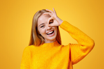 Wall Mural - Everything is ok. Cheerful teen girl showing ok sign, gesturing with fingers near her eye, orange background