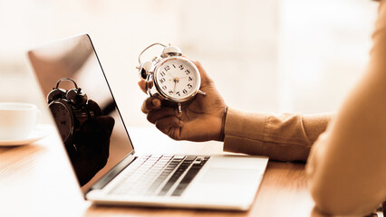 Time Management Concept. Black businessman holding alarm clock, working on laptop. Panorama, copy space