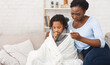 © Prostock-studio - Flu Concept. Worried black mother checking her daughter's temperature, child covered in blanket, copy space