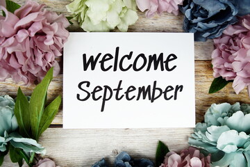 Wall Mural - Welcome September text on paper card with flowers frame top view on wooden background