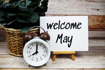 Sticker - Welcome May text on paper card with alarm clock on wooden background