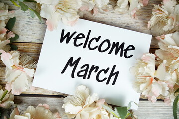 Wall Mural - Welcome March text on paper card with flowers frame top view on wooden background