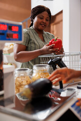 Wall Mural - Happy black woman shops at a local food market for fresh, organic produce. She smiles as the shopkeeper helps her weigh her fresh produce. There are a variety of vegetables available.