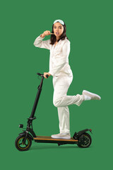 Poster - Young woman in pajamas with electric scooter brushing teeth on green background