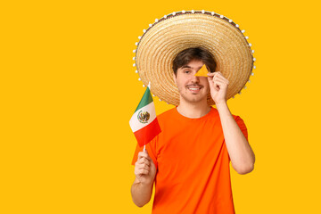 Sticker - Portrait of young man with sombrero, flag of Mexico and tortilla chip on yellow background. National Tortilla Chip Day celebration