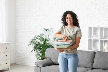 Poster - Beautiful young happy African-American woman with stack of clean clothes at home