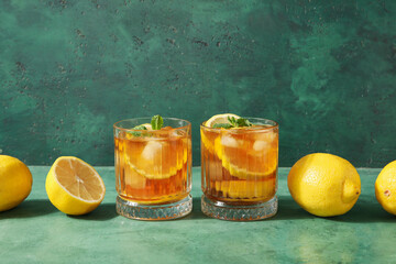 Glasses of tasty cold ice tea and lemons on green grunge background