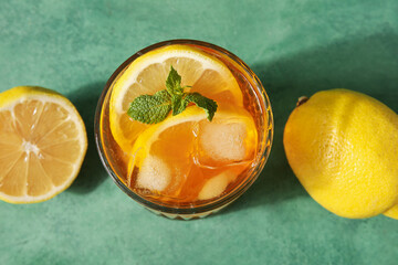 Wall Mural - Glass of tasty cold ice tea and lemons on green grunge background, closeup