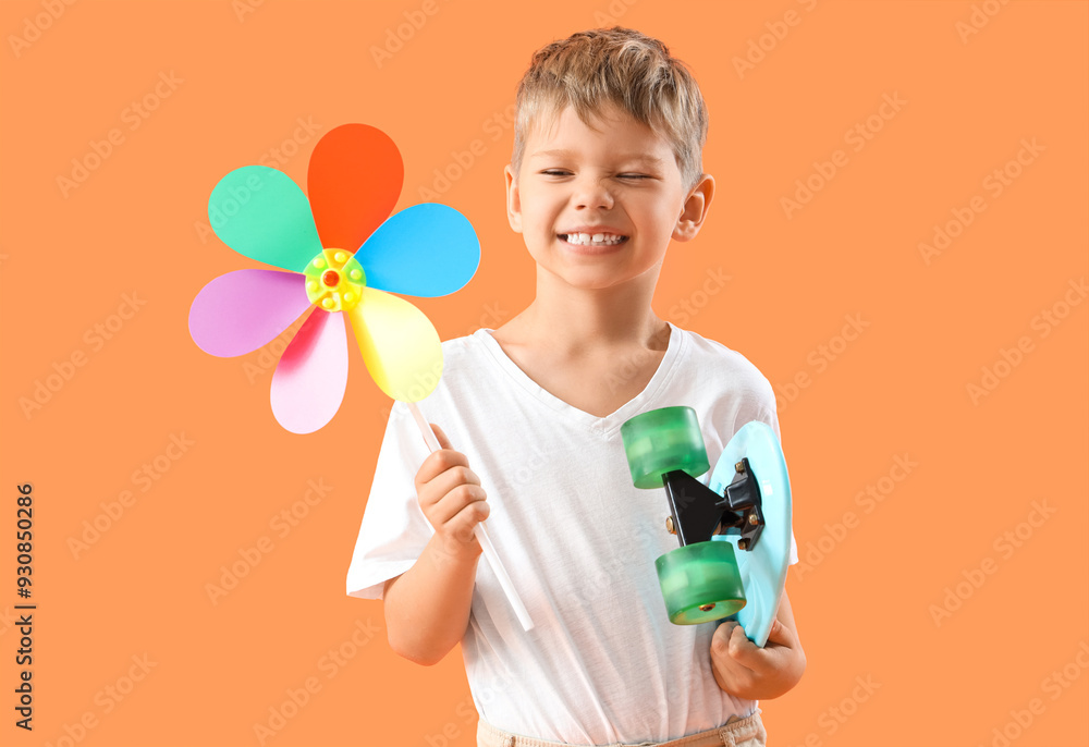 Cute little boy with toy windmill and skateboard on orange background