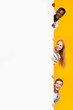 © Prostock-studio - Three multiracial students hiding behind empty board for advertising, yellow studio background