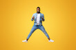 © Prostock-studio - Happy african american man jumping in air with his thumbs up over yellow studio background with free space