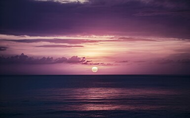 Wall Mural - Sunset over the ocean with sky transitions from deep purples, warm pinks and oranges in the horizon.