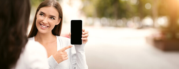 App recommended share information concept. Cheerful woman showing her friend blank smartphone screen, empty space for mockup