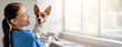 © Prostock-studio - Smiling veterinarian in blue scrubs holds a joyful Jack Russell Terrier, ensuring the pet's comfort during a routine checkup in a sunny clinic room