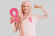 © Pixel-Shot - Young Muslim woman with pink ribbons showing muscles on light background. Breast cancer awareness concept
