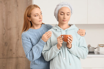 Sticker - Sad young woman after chemotherapy with coffee cup and her mother in kitchen