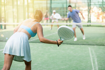 Wall Mural - Rear view of young woman in skirt playing padel tennis on court. Racket sport training outdoors.