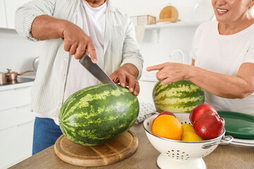 Wall Mural - Mature couple cutting watermelon in kitchen, closeup