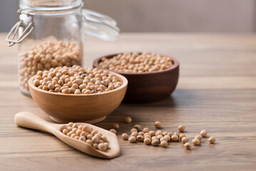 Poster - Soy bean seeds in wooden bowl, glass jar and spoon on wooden background