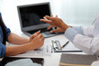 © Kansuda - Doctor and patient sitting near each other at the wooden desk in clinic. Female physician's pointing to a records form. Medicine concept