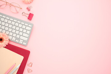 Wall Mural - Feminine home office desk table with keyboard, paper notebook, flowers on pink background. Flat lay, top view.