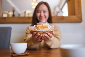 Wall Mural - Blurred  image of a young woman holding and serving a piece of cinnamon roll with coffee cup on the table