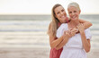 © Lumeez23/peopleimages.com - Portrait, beach and senior mom with daughter for bonding holiday, love and embrace on weekend travel. Nature, mother and woman smile on ocean adventure together with hug, fun and vacation with mockup