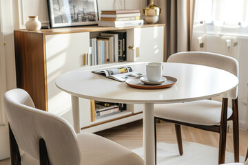 Elegant white round table set for two in a sunlit modern dining room, featuring a magazine and cup. Great for concepts of minimalistic interiors, cozy home settings, and contemporary furniture design.