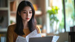 © Chatchanan - Asian woman managing finances online, reviewing bills and income on her laptop at