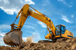 © StokHunt - A yellow excavator on an open construction site. The bucket digs the ground. Industrial image.