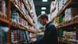 © Chatchanan - Employee in a warehouse managing inventory using a computer, with shelves of products
