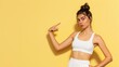 © RDO - A fit woman gesturing to her upper right, isolated on a pale yellow background, in a standard gym outfit, her stance strong yet inviting.