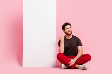 Wall Mural - Full size photo of nice man dressed brown t-shirt red pants sit indicating at white wall empty space isolated on pink color background