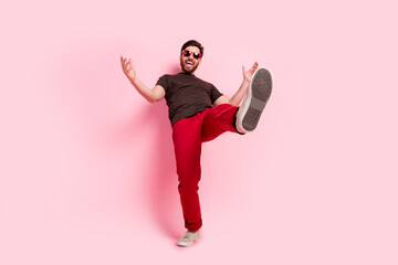 Sticker - Full size photo of positive man with stylish bristle dressed brown t-shirt in sunglass dancing show foot isolated on pink color background