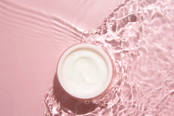 Wall Mural - Cosmetic product. Jar with cream in water on pink background, top view