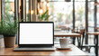 © BetterPhoto - Open laptop with a blank screen on a wooden table in a cozy café. The warm lighting and surrounding plants create a comfortable and inviting workspace atmosphere.