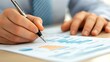 © PondLord - Close-up of a financial advisor's hands working on a financial plan with charts and graphs on the table, light solid color background