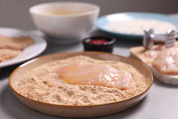 Poster - Making schnitzel. Plate with raw slice of meat in bread crumbs on grey table, closeup