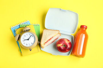 Sticker - Lunch box with snacks, bottle of juice, alarm clock and books on yellow background, flat lay